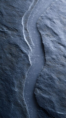  Textured dark stone surface with a narrow stream of water flowing through, highlighting natural patterns and contrasts in the geological formation and landscape