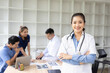 © SOMKID - A young female doctor smiling looking at the camera in meeting room, Medical team reviewing data.
