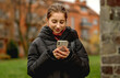 © tan4ikk - Smiling Girl Holding A Smartphone Against A Blurred City Background In Spring