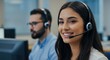 © MstShilpi12 - Smiling young woman wearing a headset engages in customer service work alongside a male colleague in a professional office environment