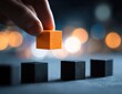 © Flux - Hand placing orange block among black ones, bokeh background