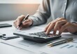 © senyumanmu - Person using a calculator at a desk with papers