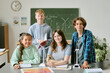 © AnnaStills - Group of multiethnic teenagers working on wind turbine models in classroom, standing and sitting at desk with charts and notebooks, smiling and looking at camera