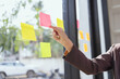 © SOMKID - young businesswoman with paper notes on glass wall working in office.