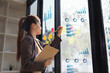© SOMKID - young businesswoman with paper notes on glass wall working in office.