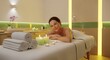 © Anelya - Woman relaxing on massage table surrounded by glowing candles in a serene spa setting at daytime enjoying wellness and self-care treatments and pampering services candles, relaxation, relaxing, serene