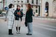 © qunica.com - Three fashionable women in conversation on a city street, embodying collaboration, style, and connection.