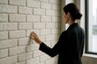 © LIDIIA - Businesswoman touching brick wall. A professional woman in a suit feels the texture of a white brick wall indoors, symbolizing a challenge or obstacle.