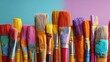 © twobrother - A vibrant array of paintbrushes, varying in size, shape, and color, stand closely together against a teal and pink backdrop, showcasing colorful paint residue on their bristles and handles