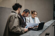 © qunica.com - Three people gather outside to discuss tasks, using a laptop and paper documents, fostering collaboration and work connections.