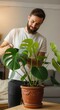 © SERHII - Smiling young man watering houseplant monstera in cozy living room