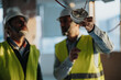 © qunica.com - Focused engineers wearing safety gear examine a smoke detector at a construction area, ensuring proper compliance with installation standards and safety protocols.