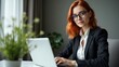 © MdAmin - Professional redhead woman with glasses working diligently on her laptop in a modern office setting with natural light