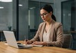 © sujon1638 - Focused professional woman wearing glasses diligently taking notes while working on a laptop at a modern office desk