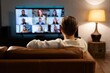 © Light Odyssey - Person watching video conference call on tv at home on couch remote work concept