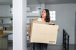 © itchaznong - Moving house. Woman carrying a box while smiling in her new home.