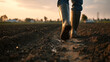 © Jhati - A person walking through a muddy field wearing rubber boots during golden hour light