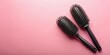 © PloyJai - Two black round hairbrushes on pink background, ideal for hair styling and grooming.  The brushes feature soft bristles for detangling and styling.