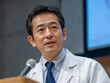 © smayakko - Male Doctor Presenting at a Medical Conference : A close-up portrait of a middle-aged Asian male doctor in a white lab coat and tie, speaking confidently into a microphone at a podium.