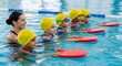 © fdp - Swimming Lesson for Kids Cheerful female instructor teaching a group of young children with kickboards in a swimming pool lesson.
