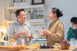© Rakchanok - Joyful Asian grandparent, bonding at home lifestyle, warm moment of elderly couple enjoying coffee conversation while grandson stands together, cozy holiday kitchen with relaxed background atmosphere