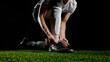© Lustre Art Group  - Soccer player tying cleats on green grass with dramatic dark background. Concept of evening football prep, focus, sport discipline, match tension, training determination.
