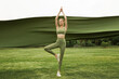 © Guoquan - Young woman practicing yoga outdoors with flowing fabric.