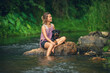 © sutlafk - Asian woman relaxing with her Rottweiler puppy on a rock in a peaceful river. Outdoor lifestyle, pet companionship, and nature getaway concept.