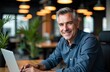 © starush - A smiling middle-aged man works on a laptop in a modern office environment