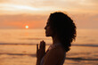 © Dina - silhouette of diverse young woman on the beach at sunrise, doing yoga, having hands in meditation namaste position, doing breathing exercise