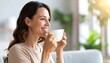 © erni - A smiling woman enjoys a warm beverage in a cozy, sunlit room