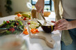 © Marko Geber - Woman slicing eggplant and vegetables on cutting board for fresh salad in sunny kitchen