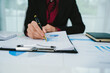 © Kieng - A businesswoman analyzes financial documents with charts and graphs at a desk, highlighting data trends with a pen in a bright, professional office setting.