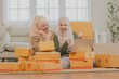 © Jestercine - Two muslim women celebrating a successful order on a laptop while managing parcels at home, showing excitement and teamwork in a thriving muslim online business.