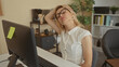 © Krakenimages.com - Woman wearing glasses and white blouse stretches neck at office desk with computer monitor; stress relief.