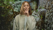 © Krakenimages.com - Woman with blonde hair making hush gesture in a park with lush green trees and stone walls in the background.