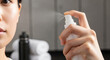 © Ace13 - A woman's hand presses the nozzle of a white spray bottle, releasing a fine cosmetic mist.