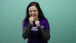 © Krakenimages.com - Woman with brunette hair in purple volunteer shirt playfully posing with fists in front of green background radiating confidence and determination.