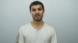 © Krakenimages.com - Young hispanic man hand covering mouth with puzzled frown and furrowed brow in pale blue studio; disgust.