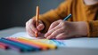 © Leninya - Focused child hand holding colorful pencil for drawing on paper. This art activity promotes creativity and education, showing moment of deep concentration
