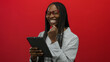 © Krakenimages.com - African woman with braids and glasses smiles and holds tablet against bright red background showing tech enjoyment and modern lifestyle.