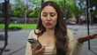 © Krakenimages.com - Woman taps smartphone screen with one hand and raises the other in a questioning gesture on street; frustration.