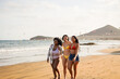 © Sabrina - Young multiracial women having fun walking on the beach during summer vacation with wind surfer in background - Holiday and travel concept