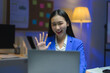 © PaeGAG - Asian businesswoman waving during video call in office at night