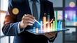 © Soyaeb - Businessman analyzing financial data on a tablet with a holographic interface showing charts and graphs for business growth.