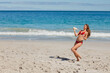 © wavebreak3 - Woman throwing flying disc on sandy beach, wearing red bikini and facing ocean waves, copy space