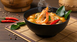 A steaming bowl of Tom Yum soup, featuring shrimp, mushrooms, and chili peppers, served on a bamboo mat.