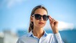© Romeo - Stylish young woman in sunglasses with confident expression on blue sky backdrop
