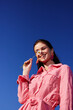 © SHOTPRIME STUDIO - Smiling female model with flower against a blue sky, wearing a pink dress, showcasing joy and summer vibes, perfect for concepts like happiness and beauty
