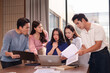 © Pichsakul - Asian business team young adults professionals facing challenging problem bad news discussing project issue looking at laptop documents serious expressions modern office meeting room
